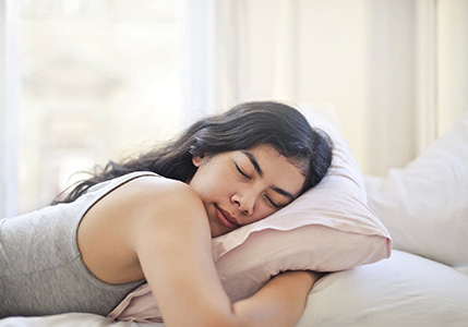 A woman in a grey tank top peacefully sleeping in a bed